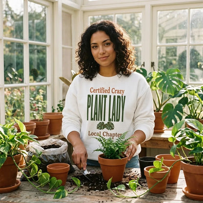 Certified Crazy Plant Lady crewneck sweatshirt — woman repotting a fern at a sunlit sunroom potting bench, White