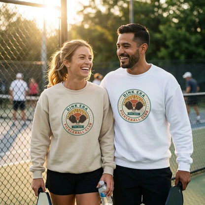 Dink Era Pickleball Club crewneck on a couple — woman in Sand, man in White — courtside golden-hour