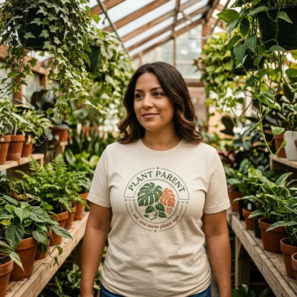 Woman in a plant-shop greenhouse wearing the Plant Parent retro botanical badge tee, full crest visible