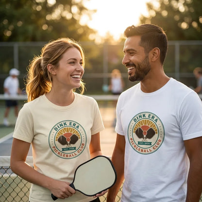 Dink Era Pickleball Club tee on a couple — woman in Natural, man in White — courtside golden-hour