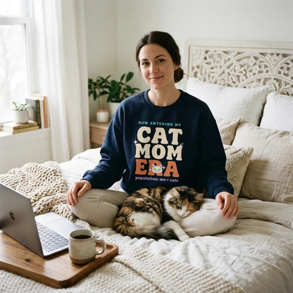 Woman relaxing on a bed in a Navy Cat Mom Era crewneck with her long-haired cat — funny cat mom sweatshirt